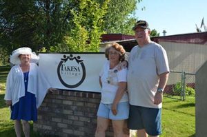 Three residents stand in front of Takesa Village community sign